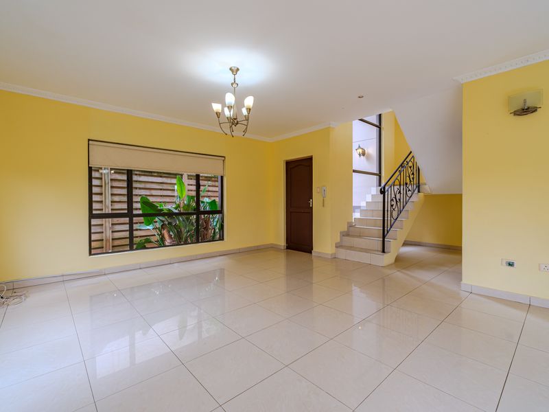 Spacious, light-filled living area featuring neutral tiled flooring, a classic staircase with wrought iron balustrade, and large windows.