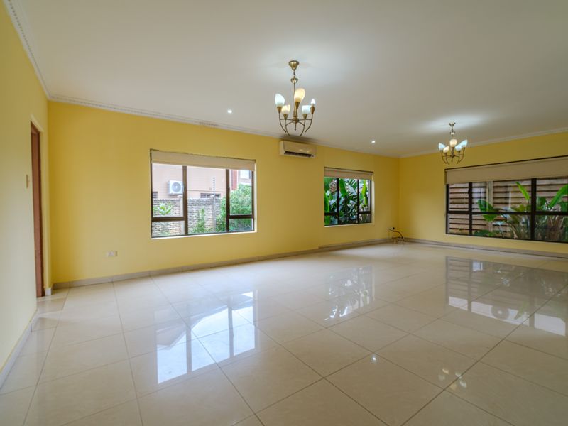 Spacious, light-filled living area featuring polished tile flooring, split-system air conditioning, and large windows with garden views.