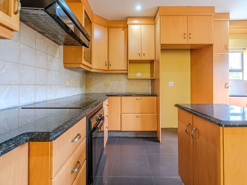A clean, functional kitchen featuring light wood cabinetry, dark granite countertops, a built-in oven and hob, and a central island.