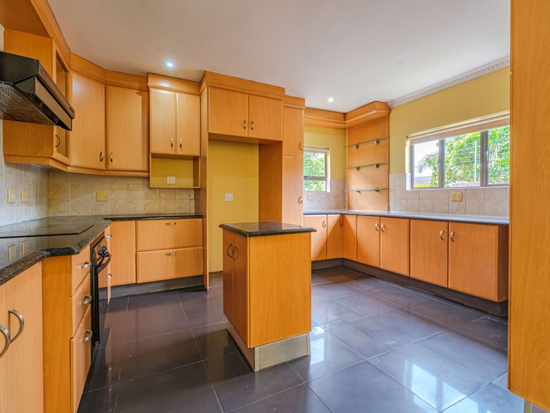 Spacious kitchen featuring light wood cabinetry, granite countertops, a central island, built-in oven, and dark tiled flooring.