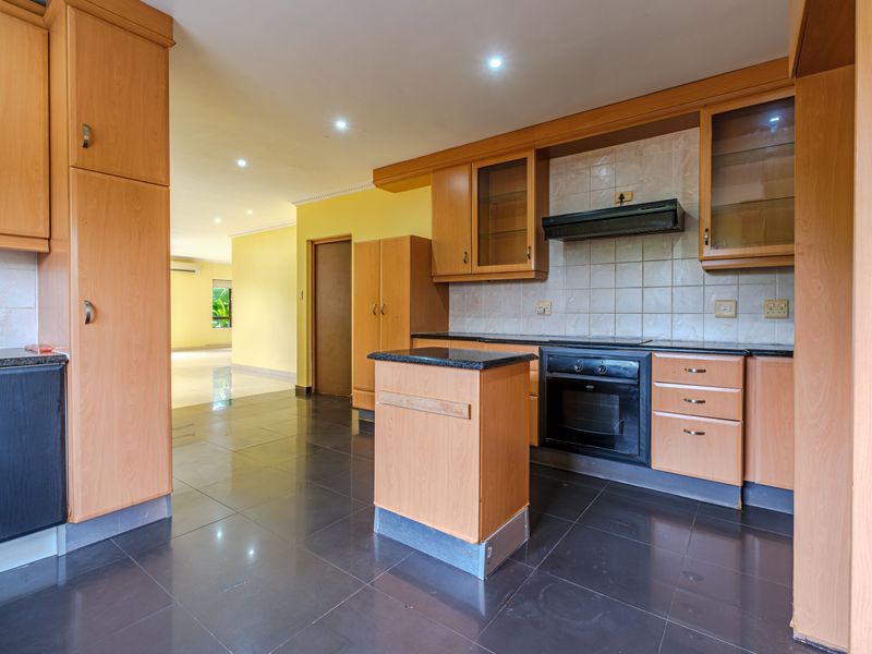 Spacious kitchen featuring light wood cabinetry, granite countertops, built-in oven, extractor fan, and dark tiled flooring, offering a functional layout for updates.