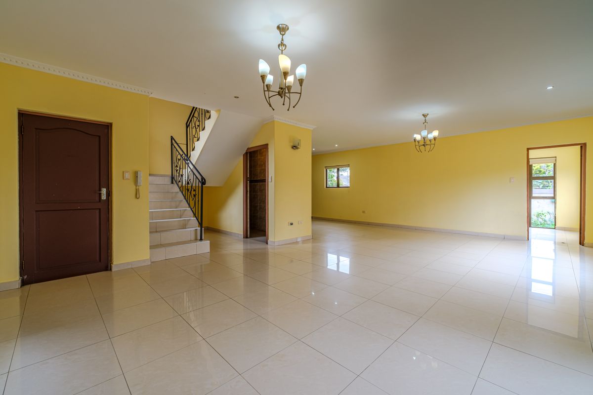 Spacious, open-plan living area featuring neutral tiled flooring, a wrought iron staircase, and bright yellow walls, offering a versatile blank canvas for interior design.