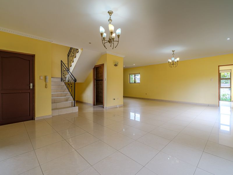 Spacious, open-plan living area featuring neutral tiled flooring, a wrought iron staircase, and bright yellow walls, offering a versatile blank canvas for interior design.