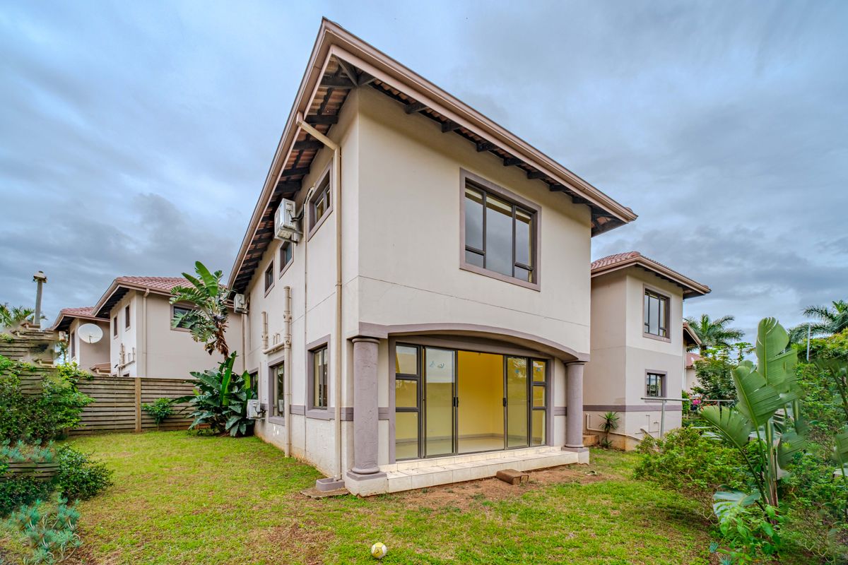 Rear view of a two-story residential house featuring a tiled roof, sliding glass doors leading to a patio, and established garden space.