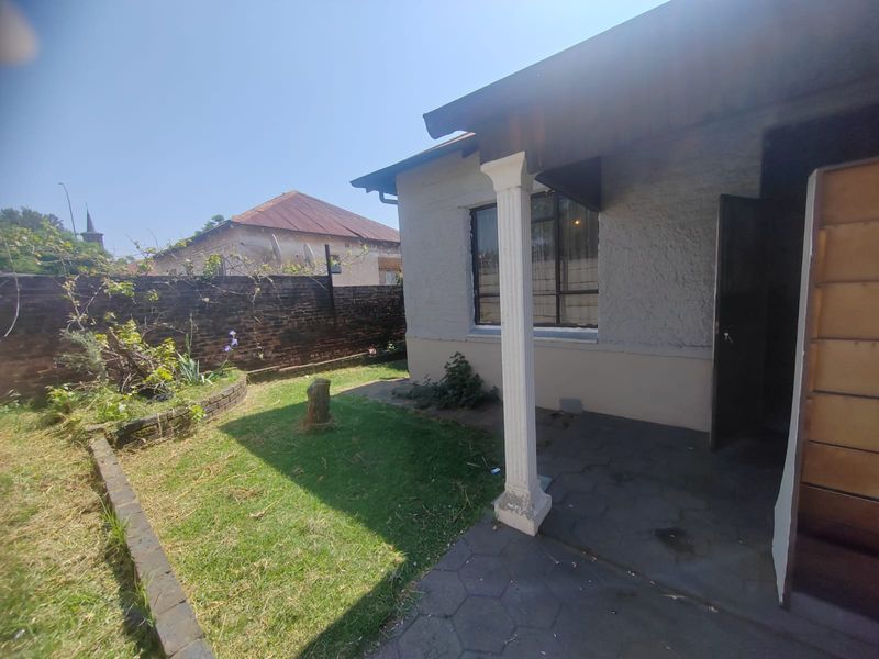 Rear exterior view featuring a paved patio area, a decorative column, and a private garden enclosed by a brick boundary wall.