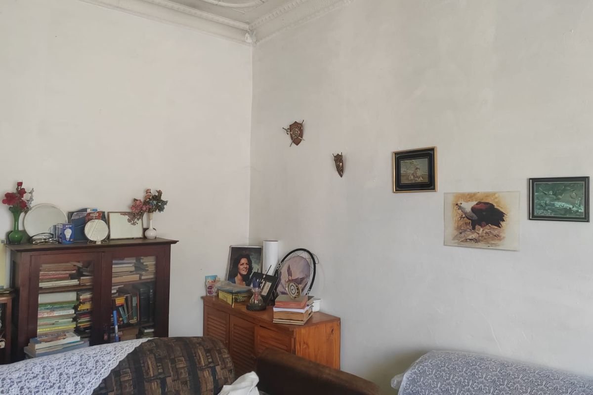 A living room featuring a classic pressed metal ceiling and ornate cornice, showing signs of wear on the wall surfaces.