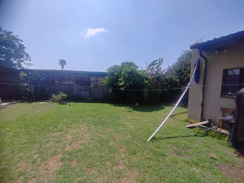 A rear garden area featuring a lawn, boundary wall, and exterior building wall with guttering and a solar panel.