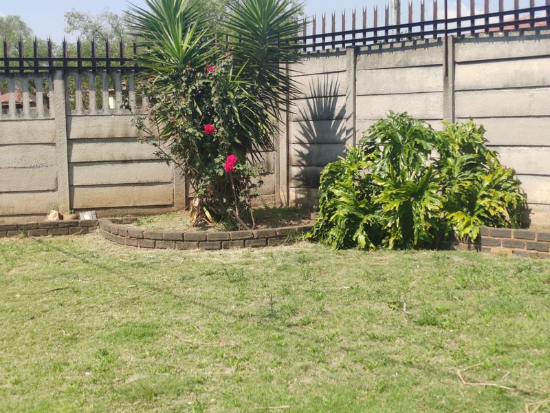 A private garden area featuring a precast concrete boundary wall with security spikes and established garden beds with brick edging.