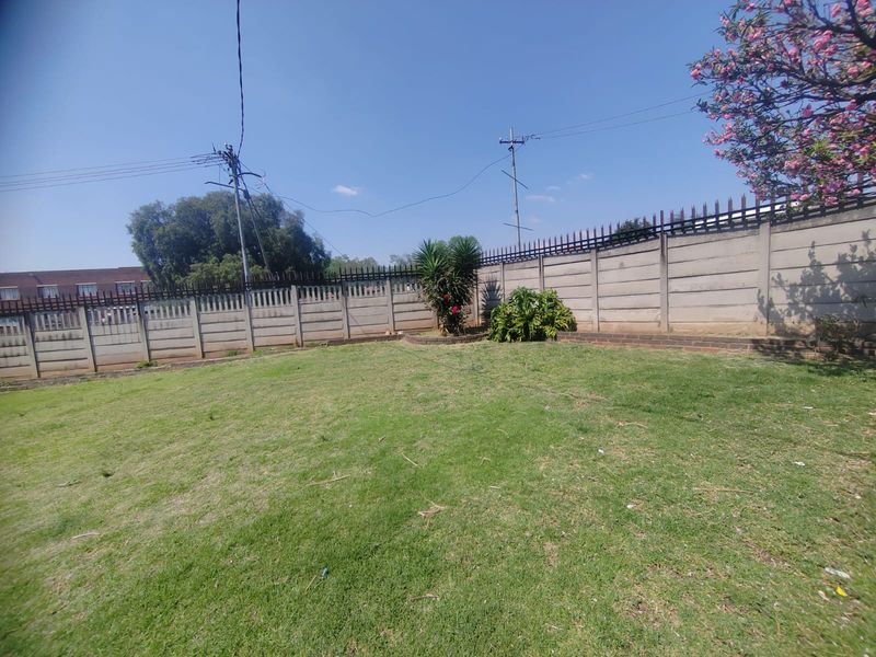 A spacious backyard featuring a well-maintained lawn enclosed by a secure precast concrete boundary wall with integrated metal security spikes.