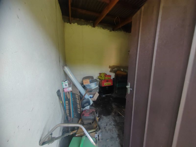 A small, unfinished utility or storage space featuring exposed timber roof beams and concrete flooring, currently used for general storage.