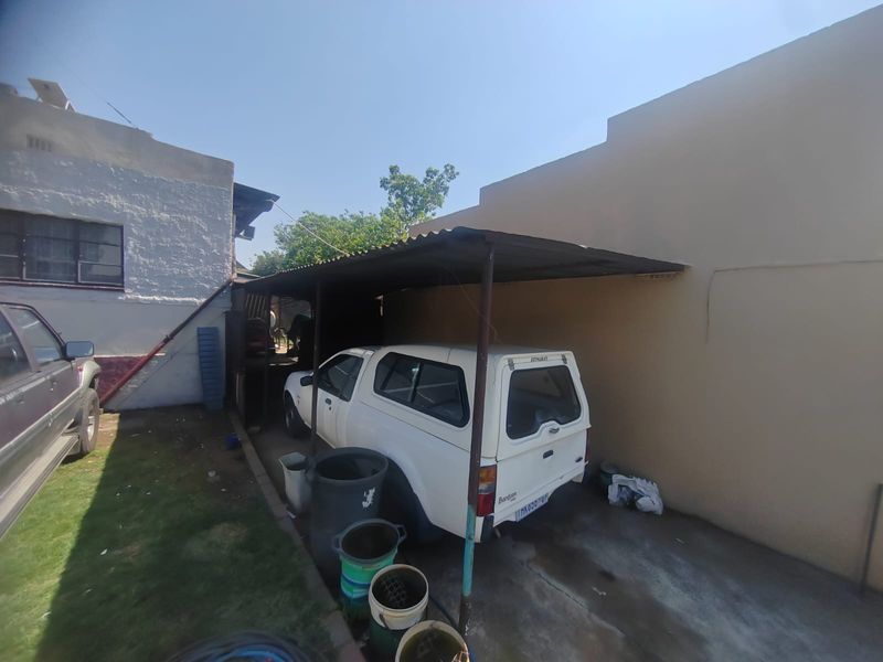 A basic outdoor carport structure with a corrugated iron roof and concrete flooring, providing covered parking space.