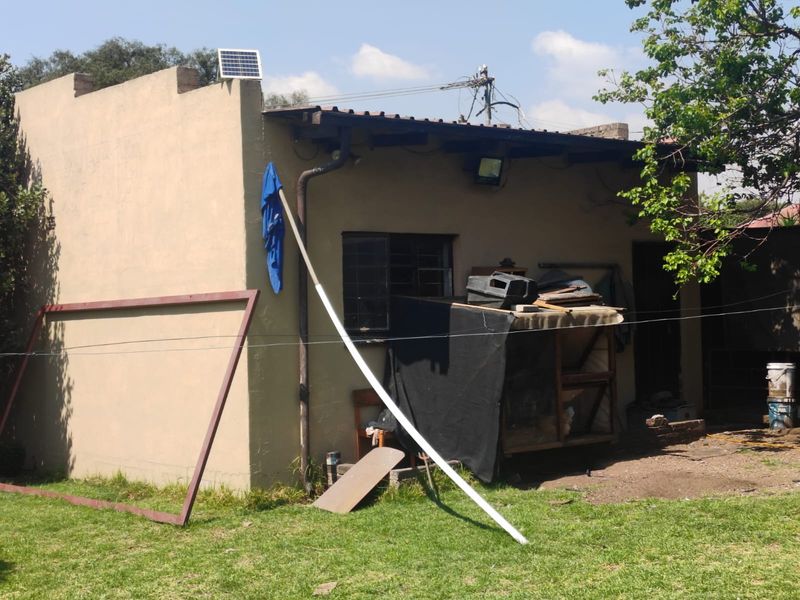 Rear view of the property showing a single-story structure with a metal roof, solar panel, and security bars on the window.