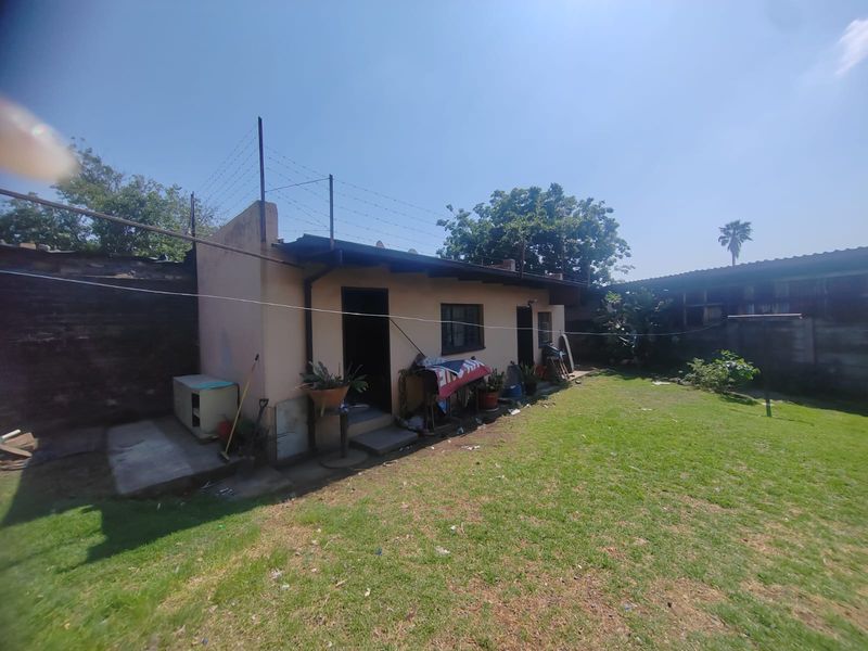 Rear view of the property featuring a lawn, concrete patio area, and perimeter brick wall with security razor wire.