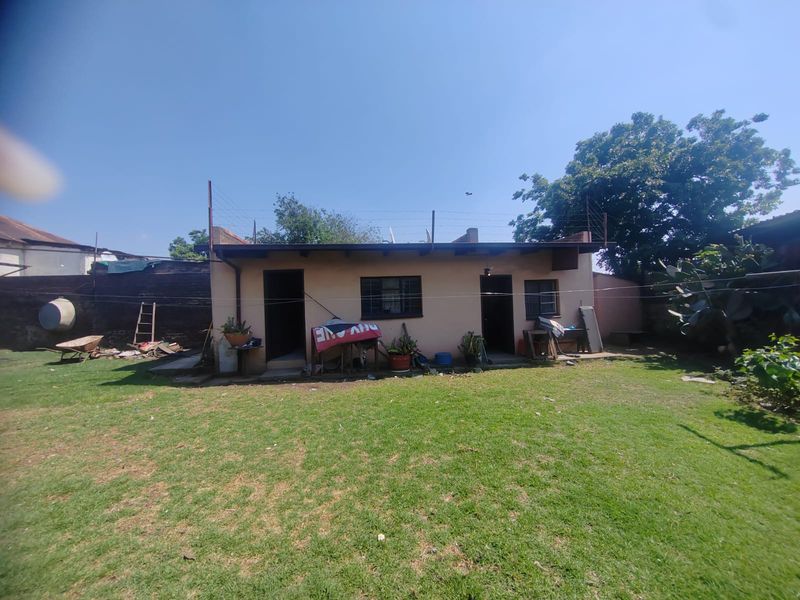 Rear view of the property featuring a lawn, security fencing, and brick boundary walls.