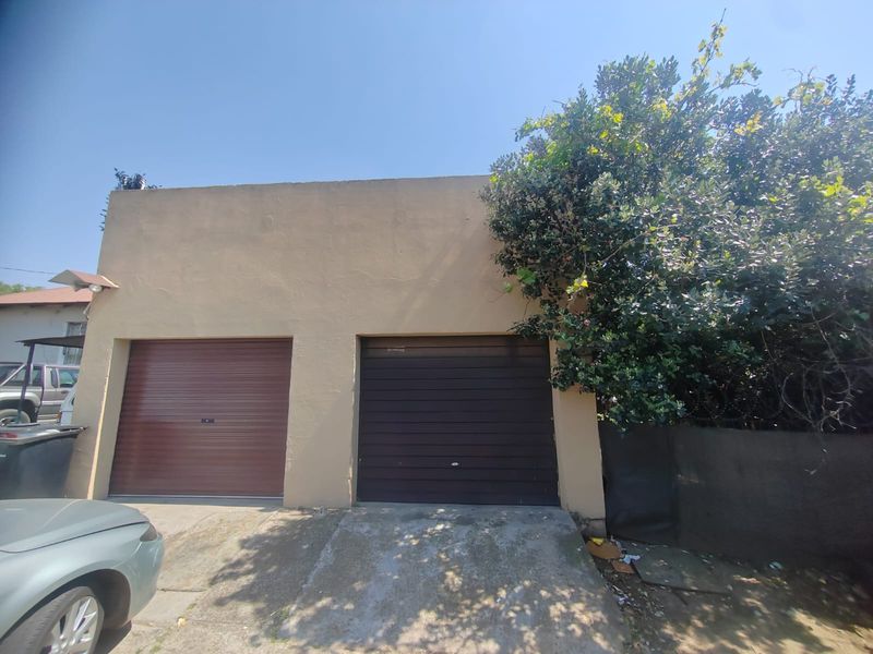A double garage with roller doors and a concrete driveway, showing signs of exterior wear.
