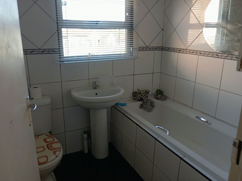 A functional bathroom featuring a pedestal basin, bathtub, and toilet with tiled walls and natural light from a window.