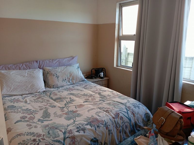 A bedroom featuring an aluminium window frame and two-tone wall finish, currently showing signs of wear and surface damage.