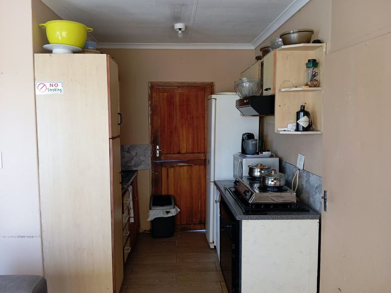 A compact kitchen featuring built-in cabinetry, tiled flooring, and a functional layout with a rear wooden door access.