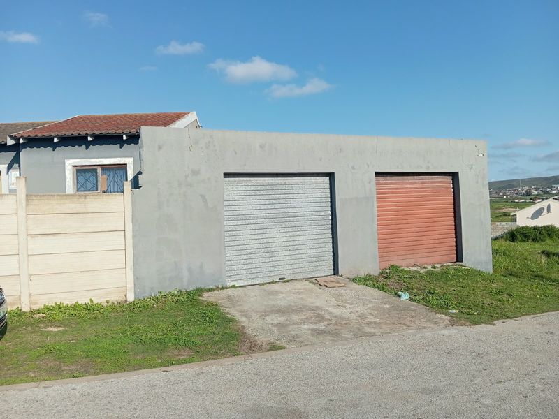 Exterior view of a double garage featuring roller doors and a concrete driveway, situated adjacent to a precast boundary wall.