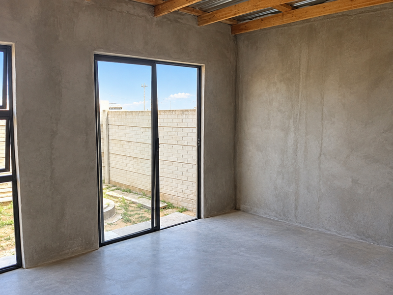 An unfinished interior space featuring exposed timber roof beams, concrete flooring, and sliding glass doors leading to an outdoor area.