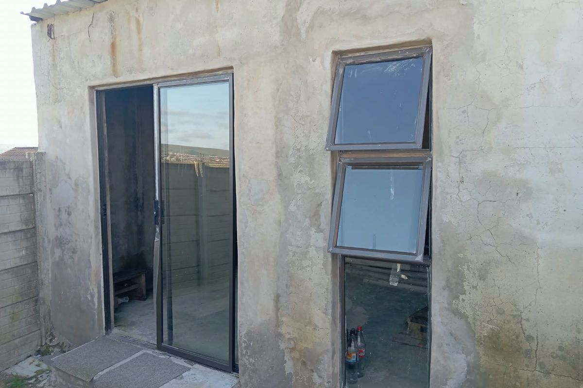 Exterior view of a rear building section featuring aluminium sliding doors and windows with unfinished, weathered concrete wall surfaces.