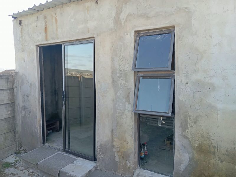 Exterior view of a rear building section featuring aluminium sliding doors and windows with unfinished, weathered concrete wall surfaces.