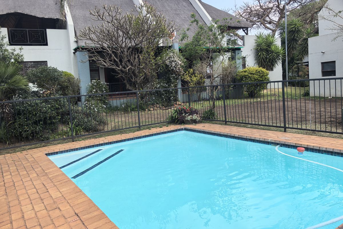 A private swimming pool with brick coping, set in a garden area in front of a townhouse with a traditional thatched roof.