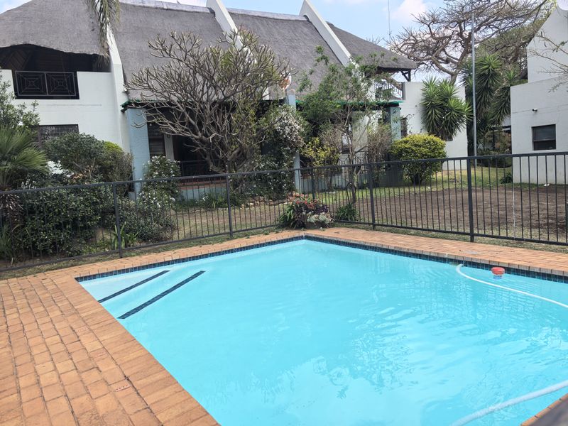 A private swimming pool with brick coping, set in a garden area in front of a townhouse with a traditional thatched roof.