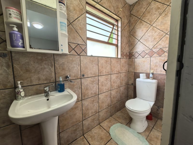 A compact bathroom featuring a pedestal basin, toilet, and full-height wall tiling. The space would benefit from modern updates to finishes and fixtures.