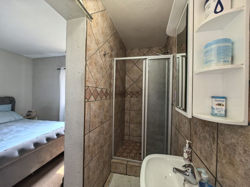 Compact en-suite bathroom featuring a tiled shower enclosure, vanity basin, and built-in shelving, conveniently located adjacent to the bedroom.
