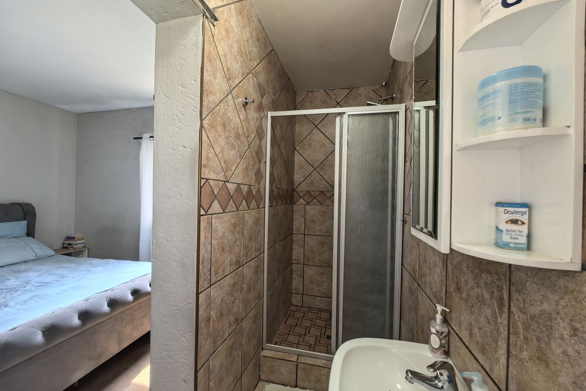 Compact en-suite bathroom featuring a tiled shower enclosure, vanity basin, and built-in shelving, conveniently located adjacent to the bedroom.