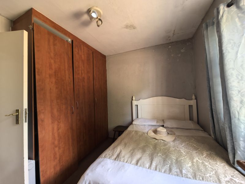 A bedroom featuring a built-in wooden wardrobe, showing signs of wear including ceiling water damage and wall surface deterioration.