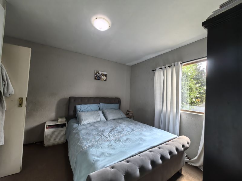 A standard bedroom featuring a built-in cupboard, neutral wall finishes, and natural light from a side window.
