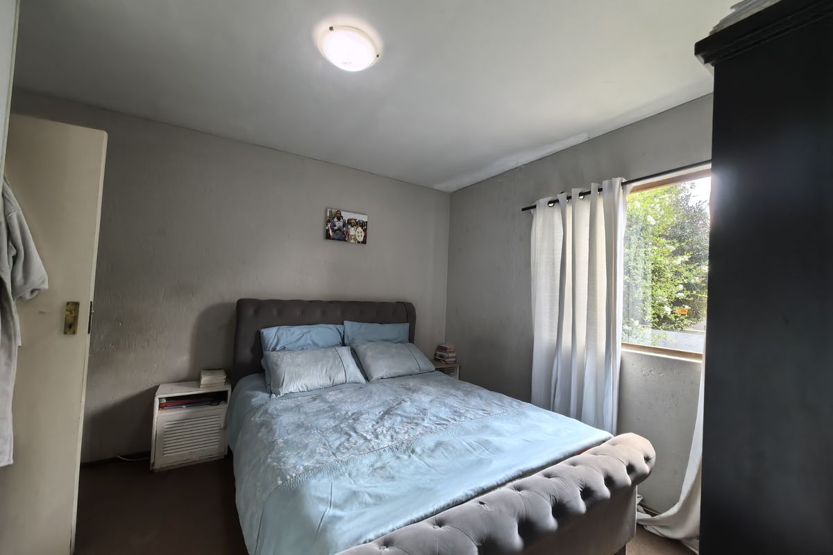 A standard bedroom featuring a built-in cupboard, neutral wall finishes, and natural light from a side window.