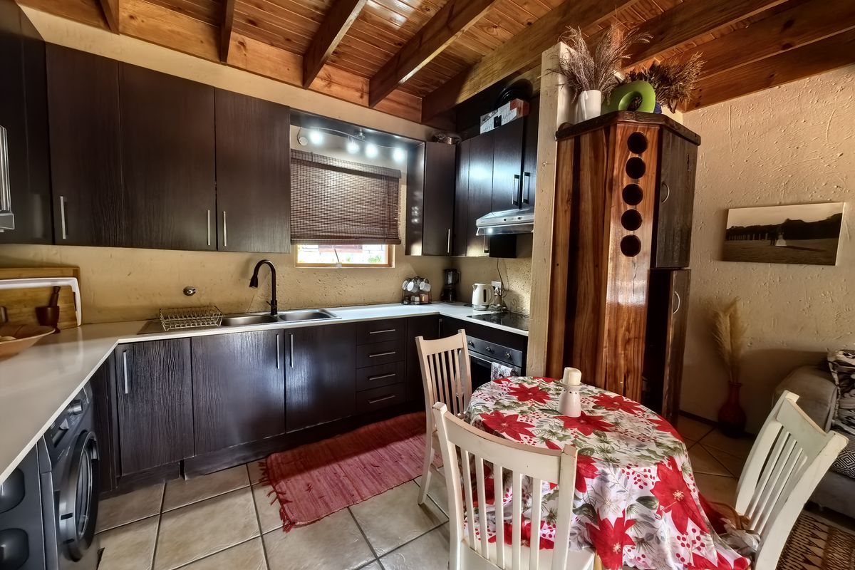 Open-plan kitchen and dining area featuring dark wood cabinetry, exposed timber beam ceilings, and tiled flooring, creating a rustic and functional living space.