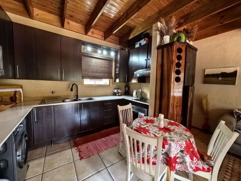 Open-plan kitchen and dining area featuring dark wood cabinetry, exposed timber beam ceilings, and tiled flooring, creating a rustic and functional living space.