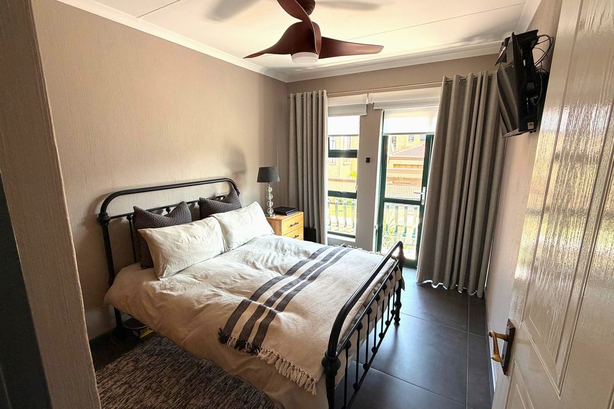 A well-maintained bedroom featuring modern tiled flooring, a ceiling fan, and direct access to a balcony through a sliding door.