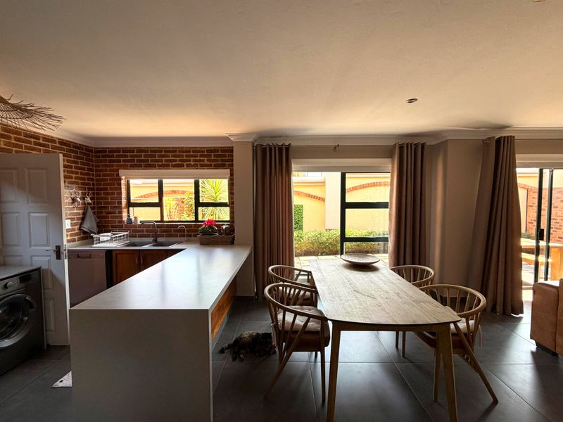 Open-plan kitchen and dining area featuring an exposed brick wall, modern kitchen island, tiled floors, and large sliding doors leading to the patio.