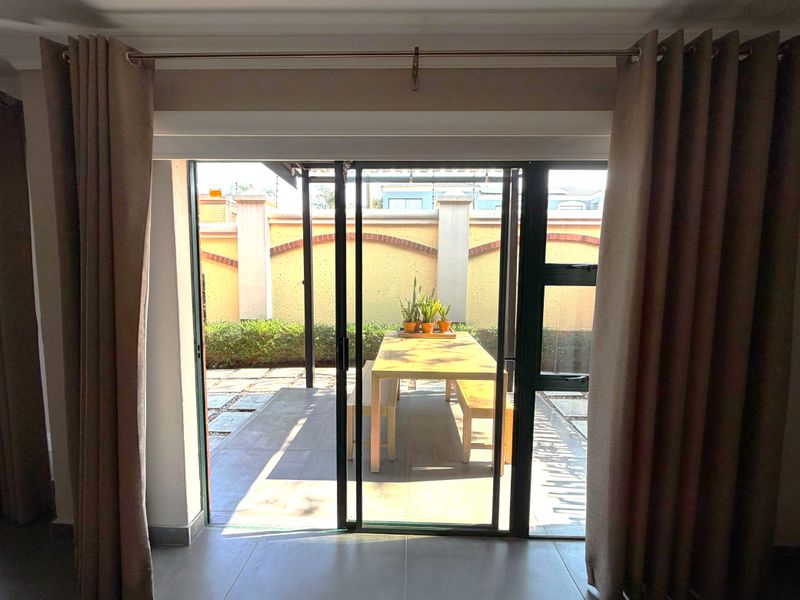 A view from the interior through sliding glass doors onto a paved patio area with a perimeter boundary wall.