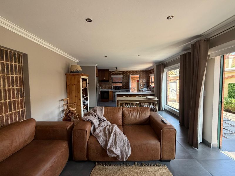 Spacious open-plan living and kitchen area featuring tiled floors, recessed lighting, and an exposed brick feature wall with direct access to the patio.
