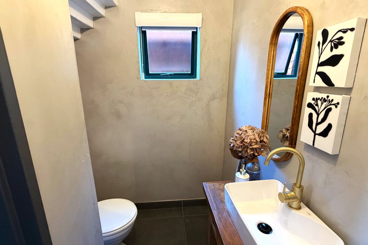 A modern guest bathroom featuring a vessel sink with brass fixtures, cement-look wall finishes, and dark floor tiles.