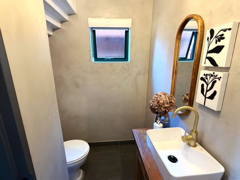 A modern guest bathroom featuring a vessel sink with brass fixtures, cement-look wall finishes, and dark floor tiles.