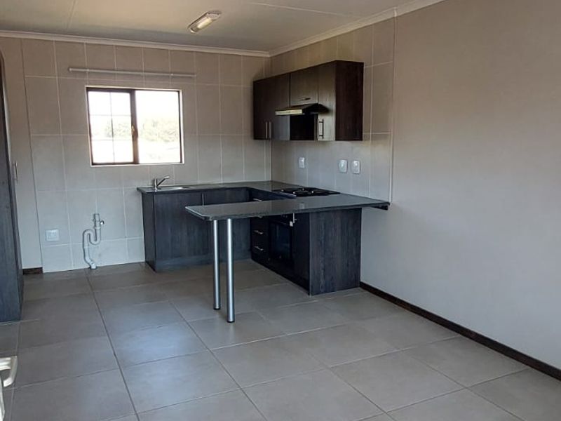 A clean, empty kitchen featuring modern dark cabinetry, tiled flooring, and a tiled backsplash, offering a functional and neutral space ready for use.