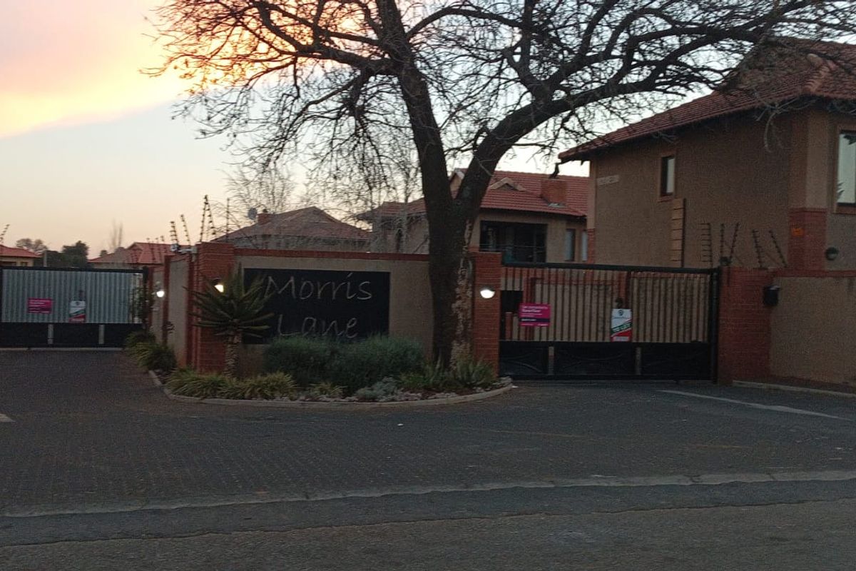 Front entrance view of the Morris Lane apartment complex featuring secure automated gates, brick boundary walls, and paved driveway access.
