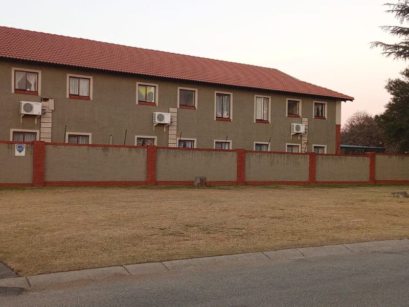 Exterior view of Morris Mews apartment complex featuring a perimeter wall with electric fencing, tiled roof, and paved driveway access.