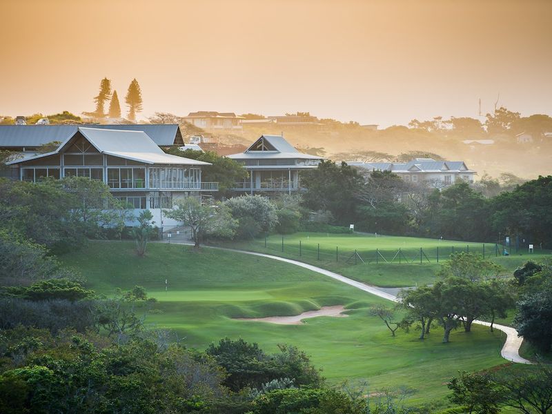 A scenic elevated view overlooking a well-maintained golf course with lush greenery and surrounding residential architecture at sunset.