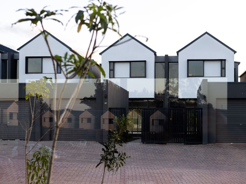 Front elevation of a modern townhouse complex featuring paved driveway, integrated garages, and contemporary architectural design.