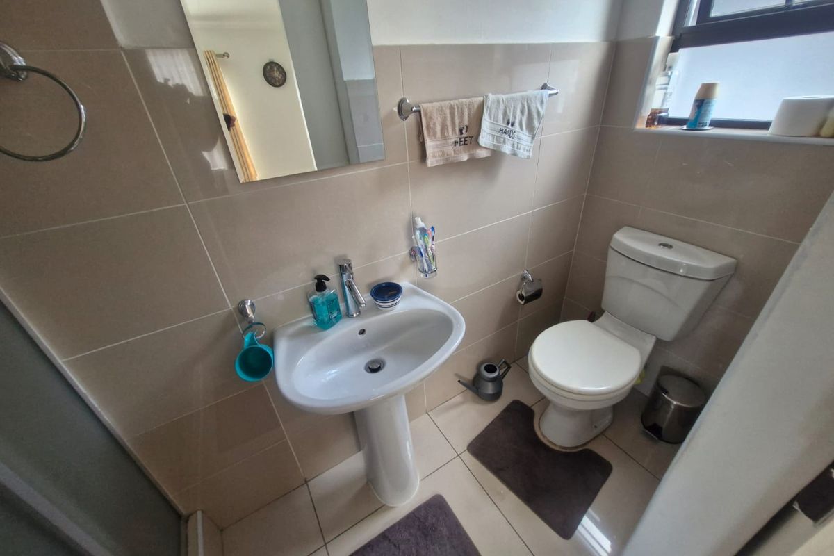 A functional bathroom featuring a pedestal basin, toilet, and neutral wall and floor tiling, providing a clean and practical space.