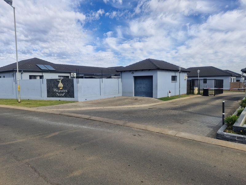 Front entrance view of Weavers Nest townhouse complex featuring paved driveway, secure gated access, perimeter walling, and garage structure.
