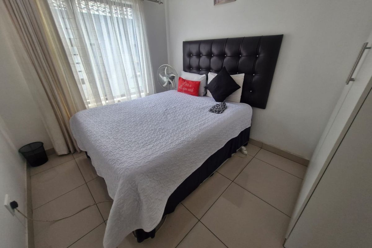 A functional bedroom featuring tiled flooring, a built-in cupboard, and natural light through a window with curtain rails.